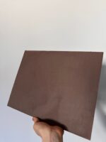 Hand holding a Marmorino sample board finished in matt mauve-brown lime plaster