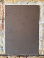 Marmorino wall panel in brown taupe with pitted stone relief, photographed straight on in a workshop