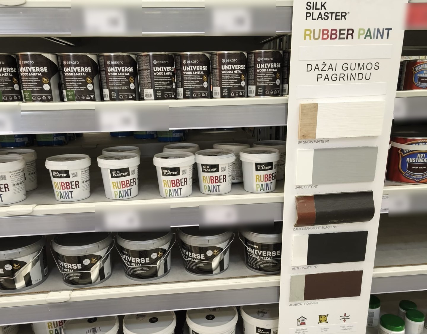 Silk Plaster Rubber Paint buckets on a DIY store shelf next to a tall display stand with painted colour samples